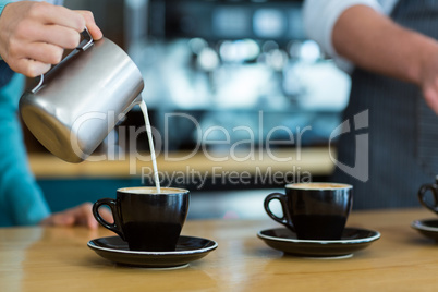 Waiter making cup of coffee at counter in cafe
