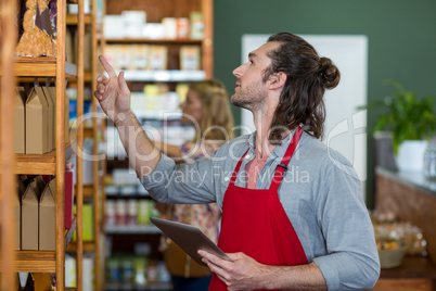 Male staff holding a digital tablet and checking grocery products on the shelf