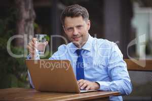Handsome businessman having drink while using laptop