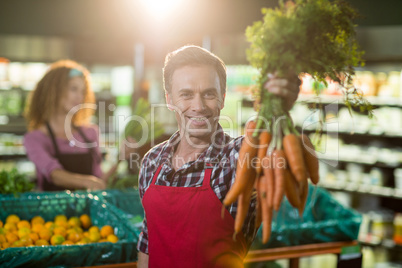 Smiling male staff holding bunch of carrots in organic section