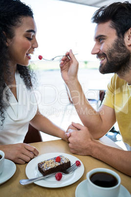 Man feeding pastry cherry to woman in coffee shop