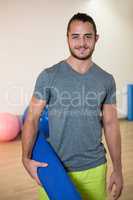 Portrait of smiling man holding rolled exercise mat
