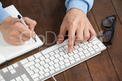 Man typing on keyboard and writing in diary