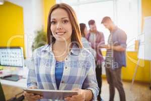 Smiling businesswoman with digital tablet standing against coworkers
