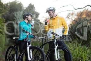 Biker couple standing with bicycle drinking water in forest