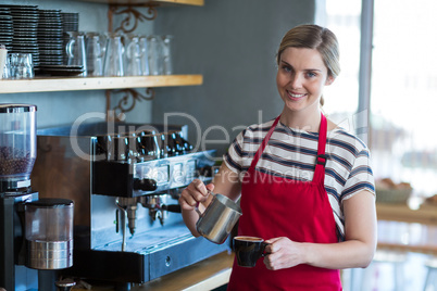 Smiling waitress making cup of coffee at counter in cafe