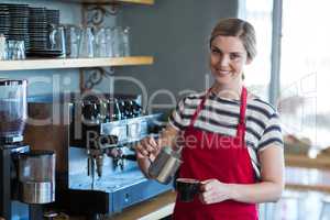 Smiling waitress making cup of coffee at counter in cafe