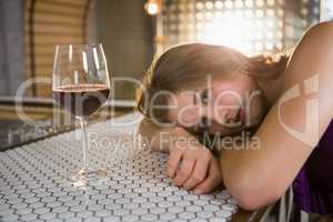 Woman lying on bar counter with wine glass on table