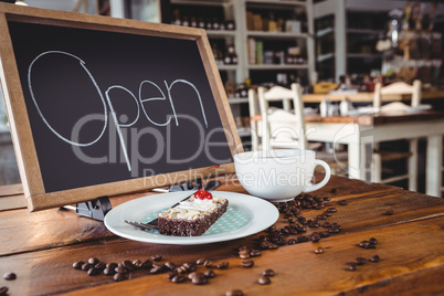 Open signboard with slice of cake and coffee cup on a table
