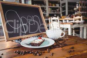 Open signboard with slice of cake and coffee cup on a table