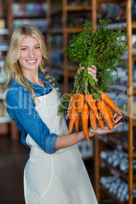 Smiling staff holding bunch of carrots in organic section