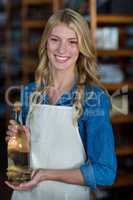 Smiling female staff holding olive oil bottle in supermarket