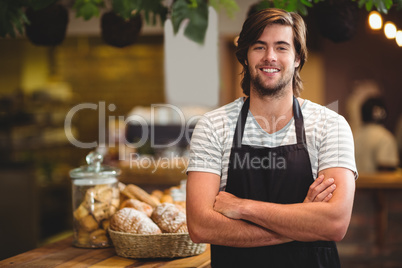 Portrait of smiling waiter standing with arm crossed