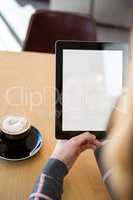 Woman using digital tablet with cup of coffee on table