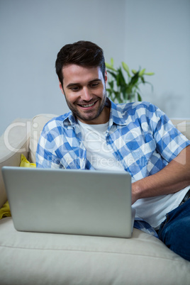 Man using laptop while relaxing on sofa