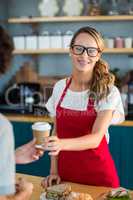 Smiling waitress serving a coffee to customer at counter in cafÃ?Â©