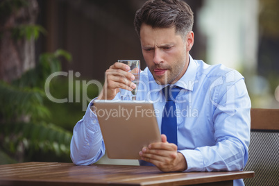 Businessman having drink while using digital tablet