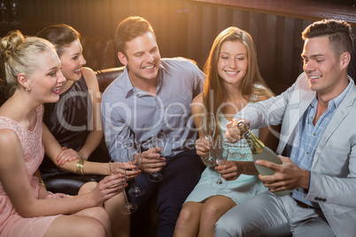 Man popping a champagne bottle while friends watching him