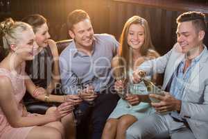 Man popping a champagne bottle while friends watching him