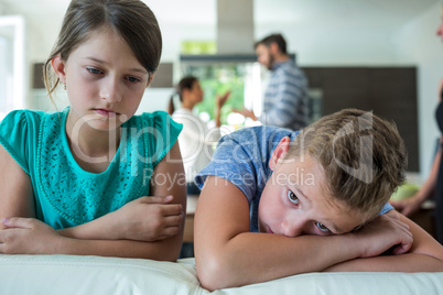 Sad kids leaning on sofa while parents arguing in background