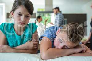 Sad kids leaning on sofa while parents arguing in background
