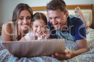 Parents lying with daughter on bed and using laptop