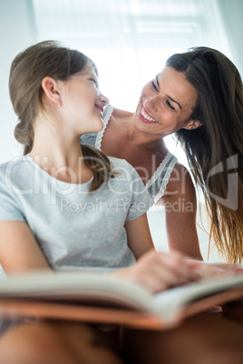 Mother and interacting daughter while reading book on bed