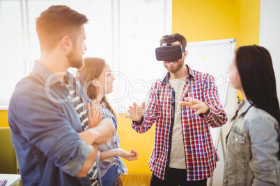 Business people looking at coworker wearing virtual reality headset