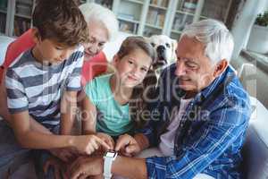 Grandparents and grandchildren looking at smartwatch in living room