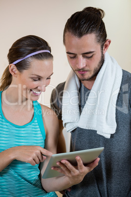 Smiling fitness trainer and woman using digital tablet