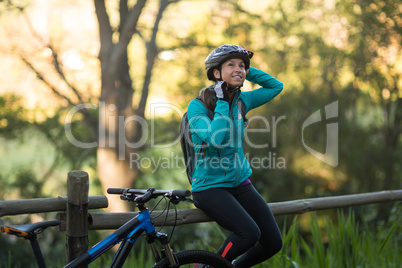 Female biker sitting on a fence and removing bicycle helmet