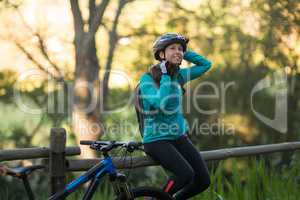 Female biker sitting on a fence and removing bicycle helmet