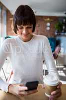 Woman using mobile phone while having coffee