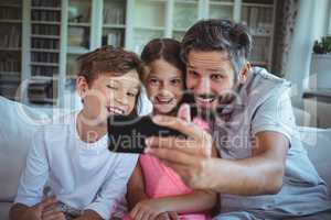 Father sitting on sofa with his children and clicking a selfie in living room