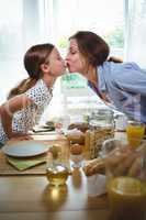 Mother and daughter kissing each other while having breakfast