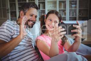 Smiling father and daughter looking at mobile phone in living room
