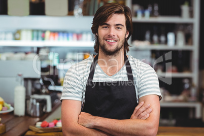 Portrait of smiling waiter standing with arm crossed