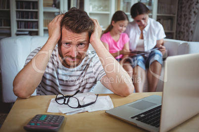 Worried man sitting at table with bills and laptop