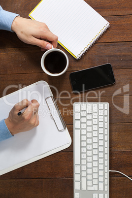 Man writing on clipboard while having cup of coffee