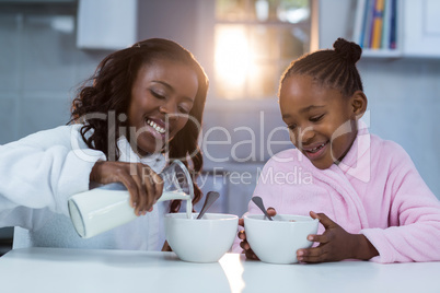Daughter looking at mother pouring milk in a bowl