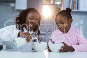 Daughter looking at mother pouring milk in a bowl