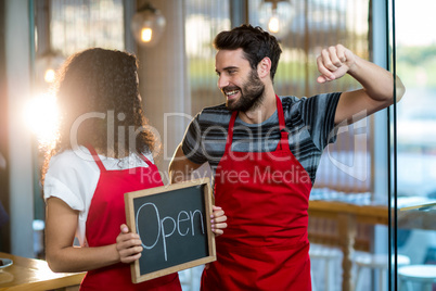 Waitress and waiter standing with open sign board in cafe