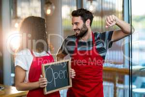 Waitress and waiter standing with open sign board in cafe