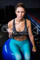 Woman with dumbbell sitting on fitness ball