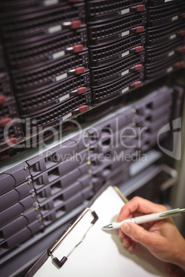 Close-up of technician maintaining record of rack mounted server on clipboard