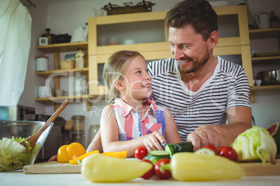 Father and daughter smiling at each other while preparing salad