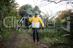 Male biker carrying mountain bike and walking on dirt track