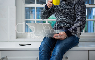 Man using laptop while having coffee in the kitchen