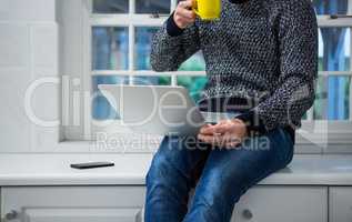 Man using laptop while having coffee in the kitchen