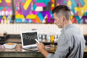 Man using mobile phone with laptop on table at bar counter